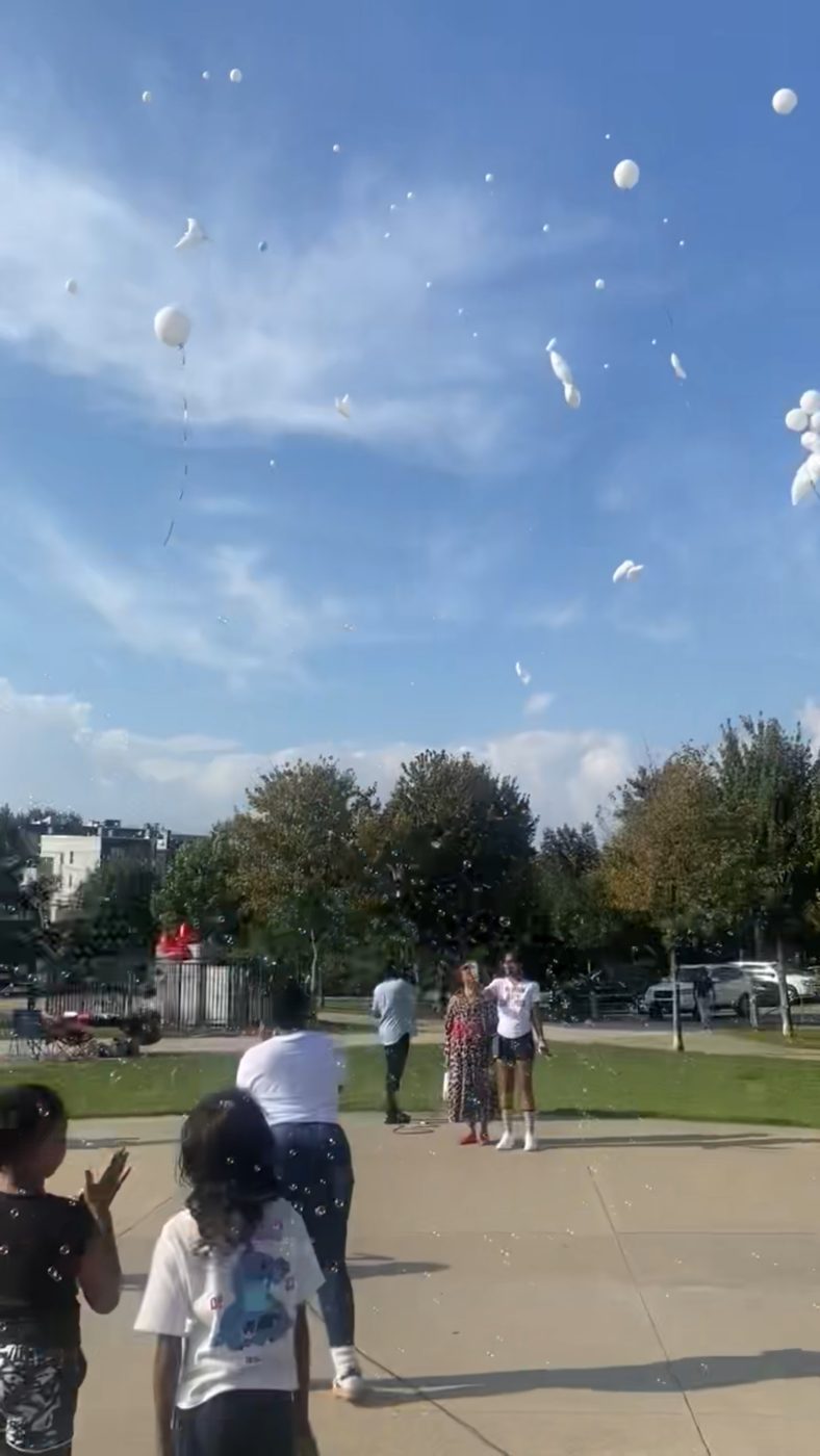 White balloons rising into a blue sky as the community watches at the memorial release