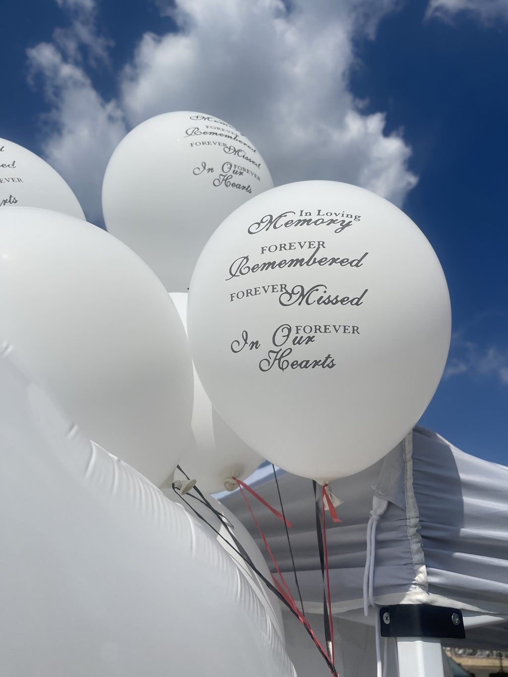 White In Loving Memory balloons against a blue sky